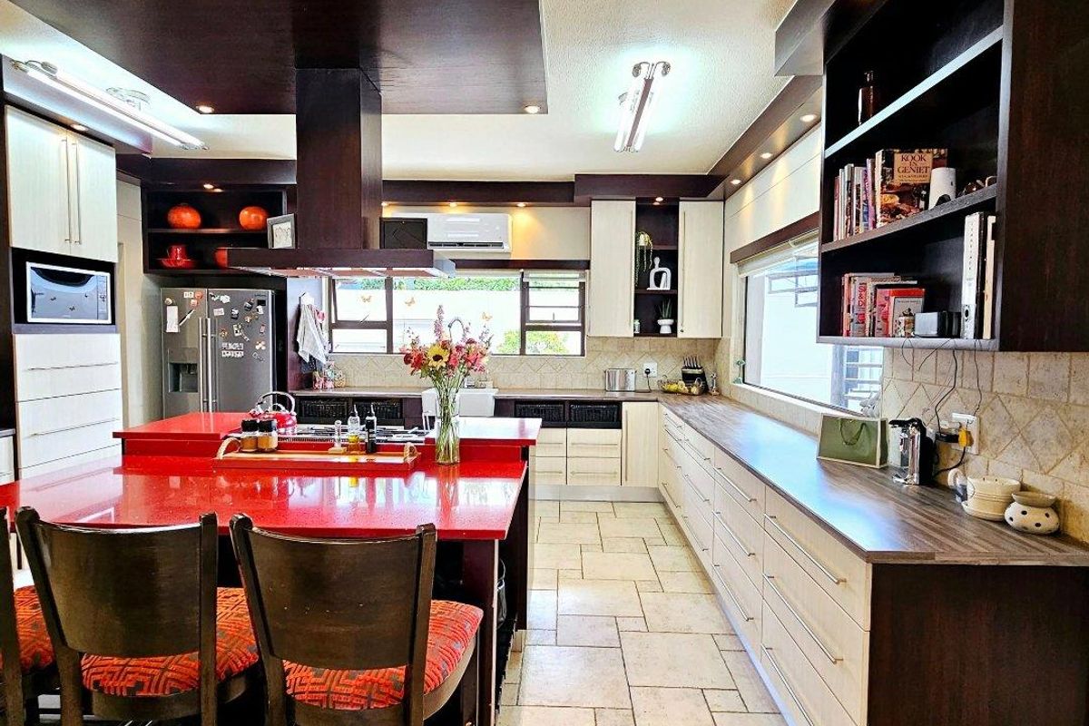 Spacious kitchen featuring a large central island with red countertops, extensive built-in cabinetry, integrated appliances, and tiled flooring with modern recessed lighting.
