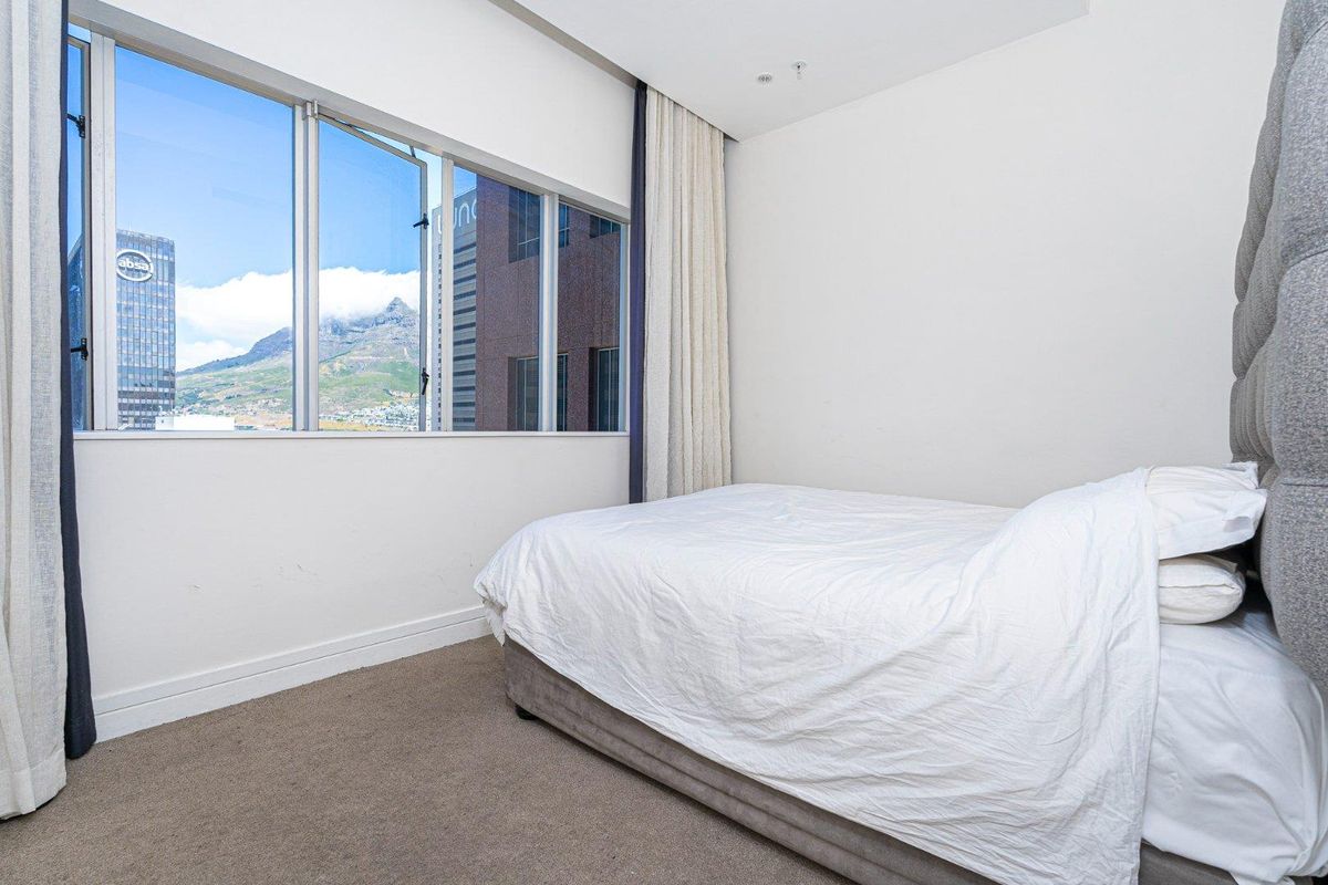 A bedroom featuring large windows with city and mountain views, neutral wall finishes, and carpeted flooring.
