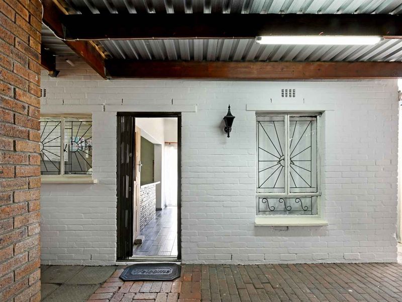 A covered patio area featuring brick paving, a corrugated metal roof, and secure access to the interior through a security gate.