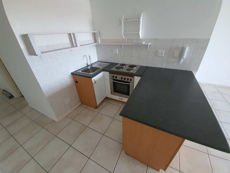 Compact kitchen featuring built-in cabinetry, a stainless steel sink, electric hob, and oven with a tiled backsplash and neutral floor tiles.