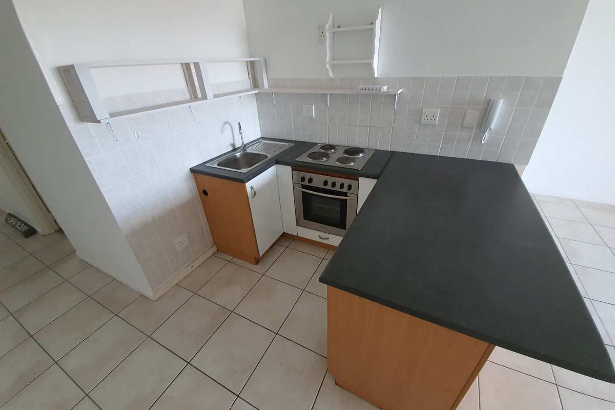 Compact kitchen featuring built-in cabinetry, a stainless steel sink, electric hob, and oven with a tiled backsplash and neutral floor tiles.