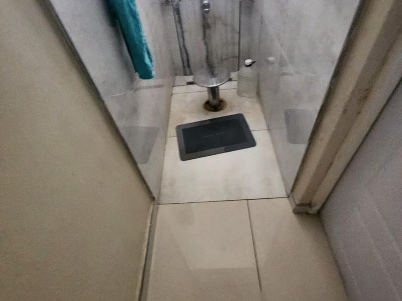 A compact shower enclosure featuring tiled walls and flooring, requiring maintenance to address visible surface wear and grout discoloration.