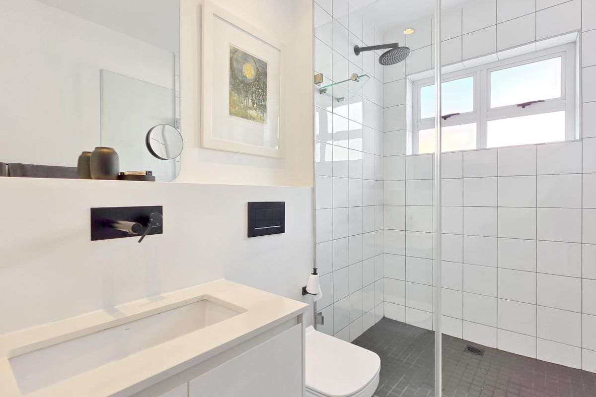 Modern bathroom featuring a wall-mounted vanity, wall-hung toilet, and a spacious walk-in shower with a glass screen and contemporary black fixtures.