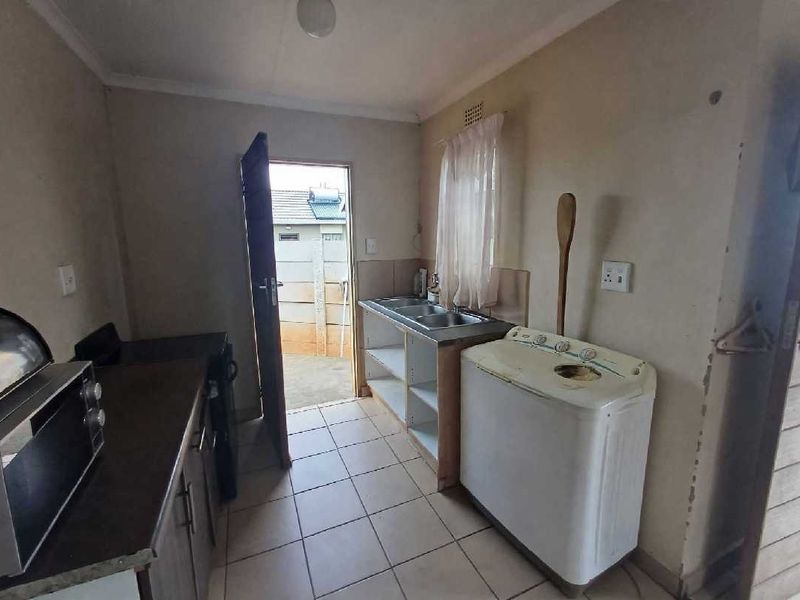 A functional kitchen area featuring tiled flooring, a double stainless steel sink, and built-in base cabinetry with direct access to the exterior.