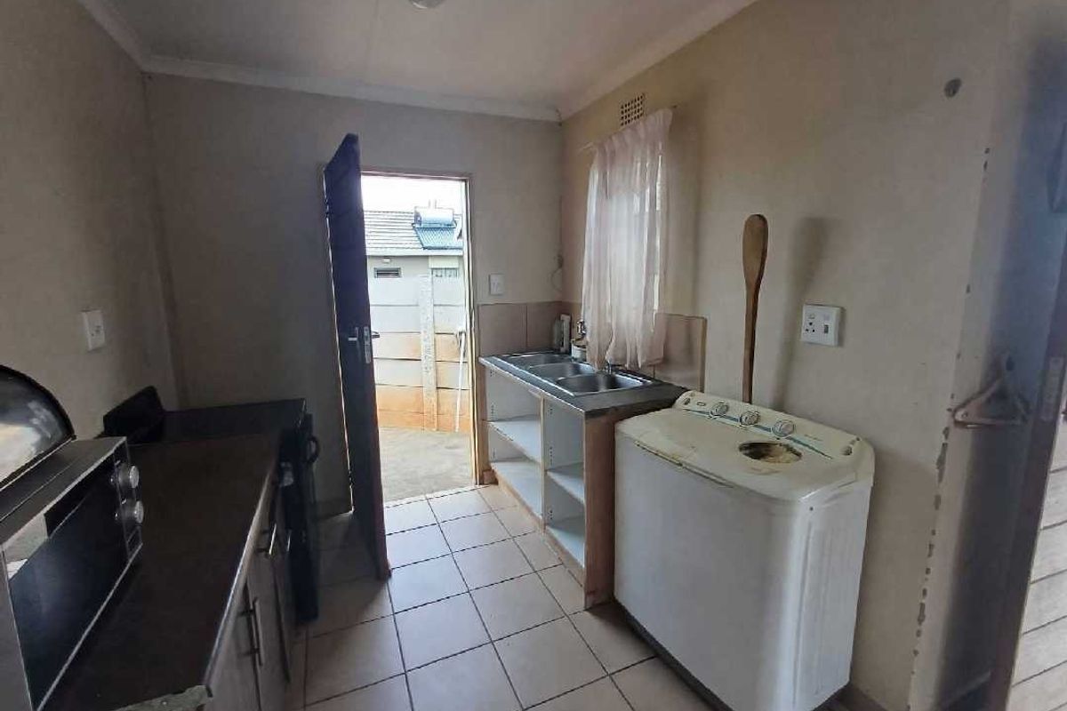 A functional kitchen area featuring tiled flooring, a double stainless steel sink, and built-in base cabinetry with direct access to the exterior.