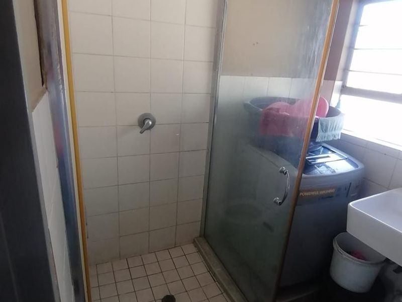 A functional bathroom featuring a shower enclosure with tiled walls and a basin, requiring some cosmetic updates to the wall finishes and shower frame.