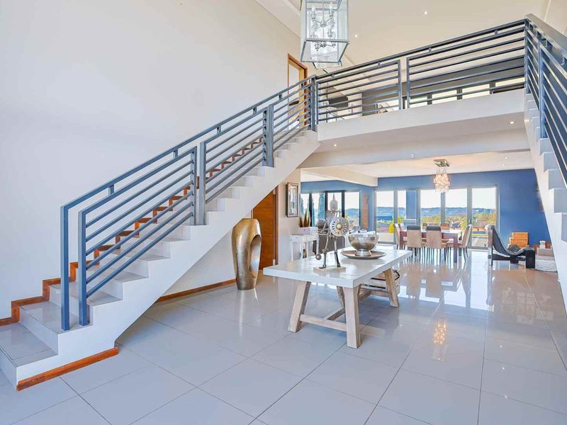 Spacious open-plan living area featuring a grand staircase with metal balustrades, mezzanine level, polished tile flooring, and expansive sliding doors leading to the outdoors.