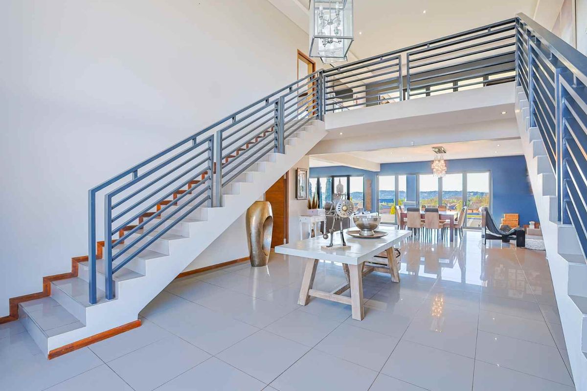 Spacious open-plan living area featuring a grand staircase with metal balustrades, mezzanine level, polished tile flooring, and expansive sliding doors leading to the outdoors.