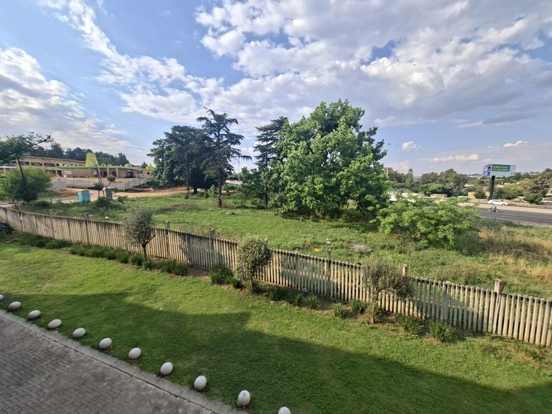 An elevated view overlooking a landscaped lawn, a picket fence, and an open green space with mature trees.