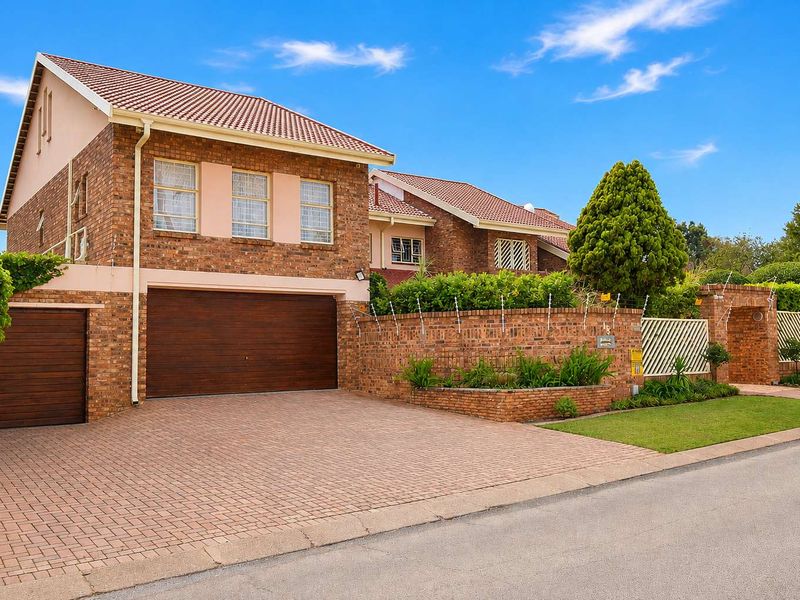 A well-maintained double-story brick home featuring a paved driveway, double garage, and secure perimeter walling with electric fencing.