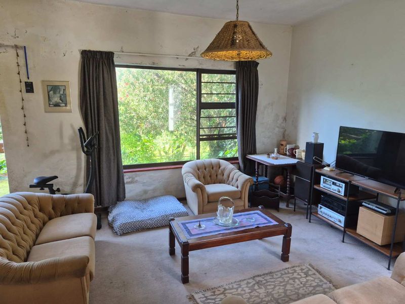 A living room featuring a large window with garden views, requiring cosmetic updates to the wall finishes.