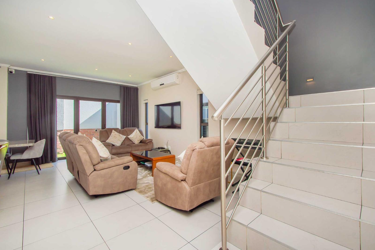 Modern open-plan living area featuring tiled floors, a contemporary staircase with stainless steel railings, and direct access to the outdoor space via sliding doors.