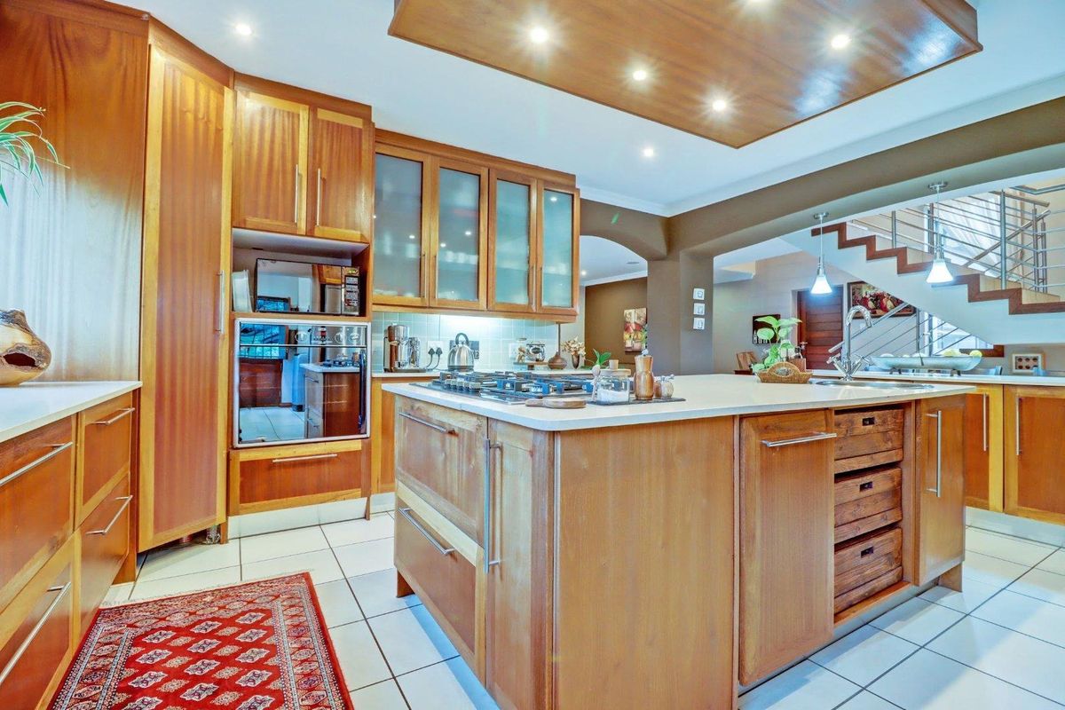 Spacious kitchen featuring warm wooden cabinetry, a large central island with a gas cooktop, integrated oven, and tiled flooring, open to the living area.
