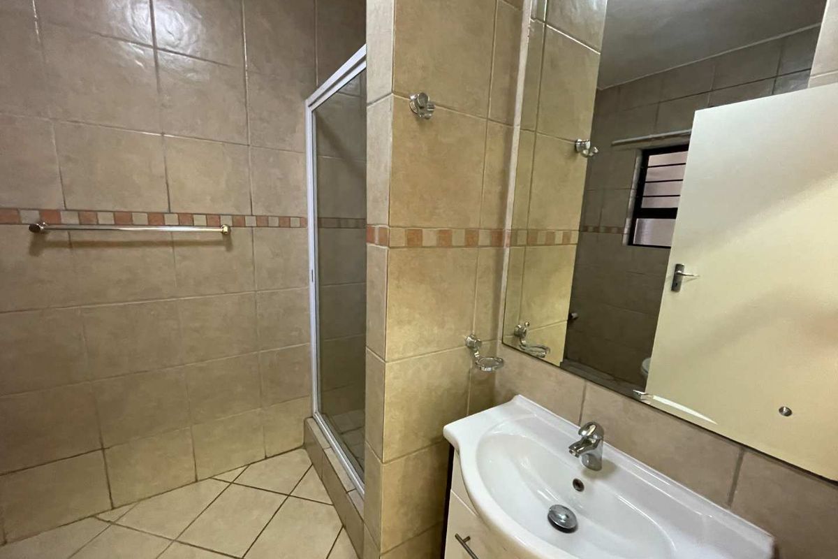 A functional bathroom featuring a tiled shower enclosure, a vanity basin with a wall-mounted mirror, and neutral wall and floor tiling.