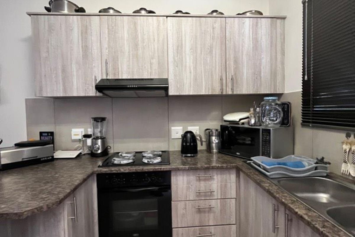 A functional kitchen featuring wood-look laminate cabinetry, dark laminate countertops, a built-in oven with hob, and a stainless steel double sink.