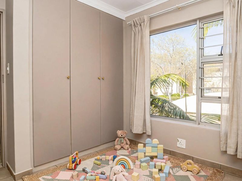 A well-maintained bedroom featuring neutral-toned built-in cupboards, large aluminium-framed windows with security bars, and coved ceilings.