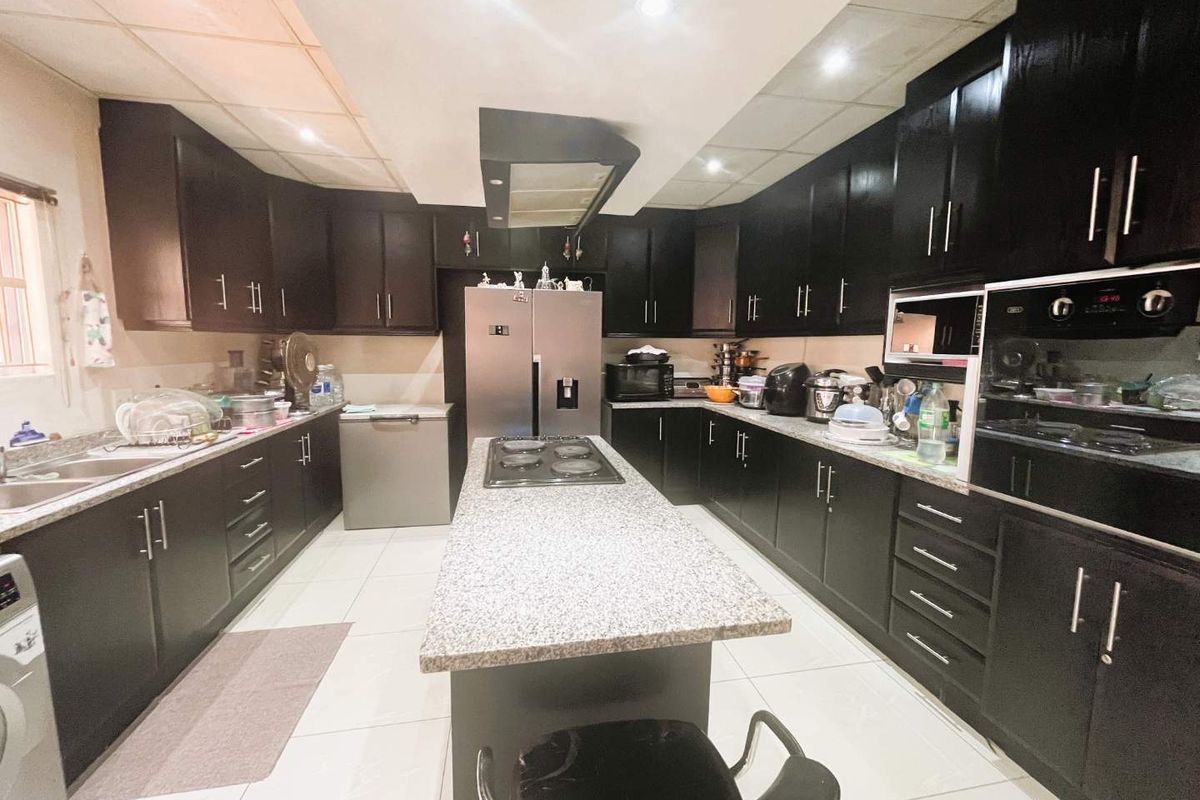 Spacious kitchen featuring dark cabinetry, granite countertops, a central island with a built-in hob, and integrated oven and microwave units.