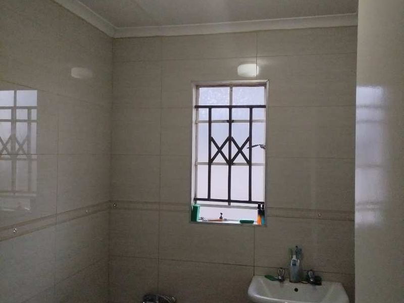 A functional bathroom featuring tiled walls, a pedestal basin, and a bathtub with a window protected by security bars.