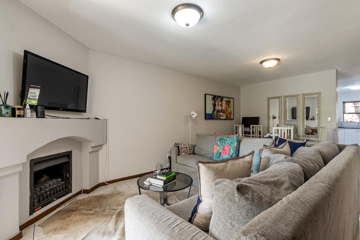A comfortable living room featuring a built-in fireplace, tiled flooring, and neutral wall finishes, with an open flow toward the kitchen area.