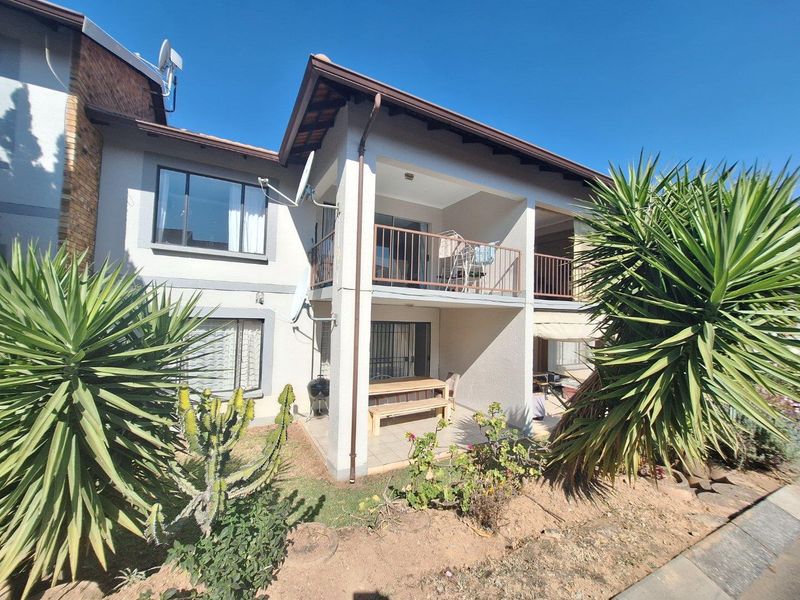 Rear view of a two-story townhouse featuring a ground-floor patio and an upper-level balcony with metal railings and tiled roof.