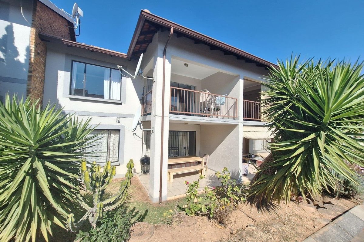 Rear view of a two-story townhouse featuring a ground-floor patio and an upper-level balcony with metal railings and tiled roof.