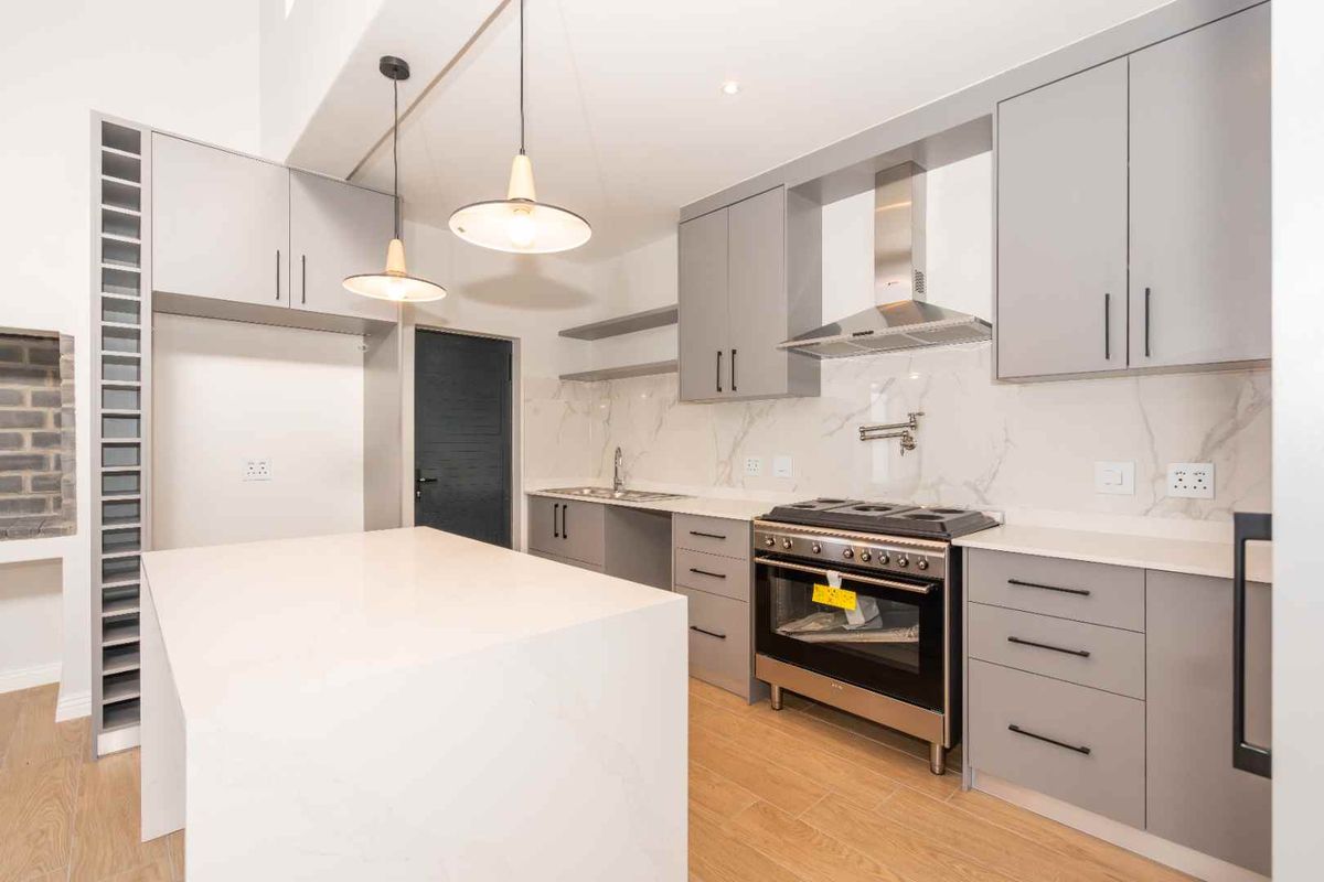 Modern kitchen featuring grey cabinetry, stone countertops, a central island, and a stainless steel gas range with an extractor fan.
