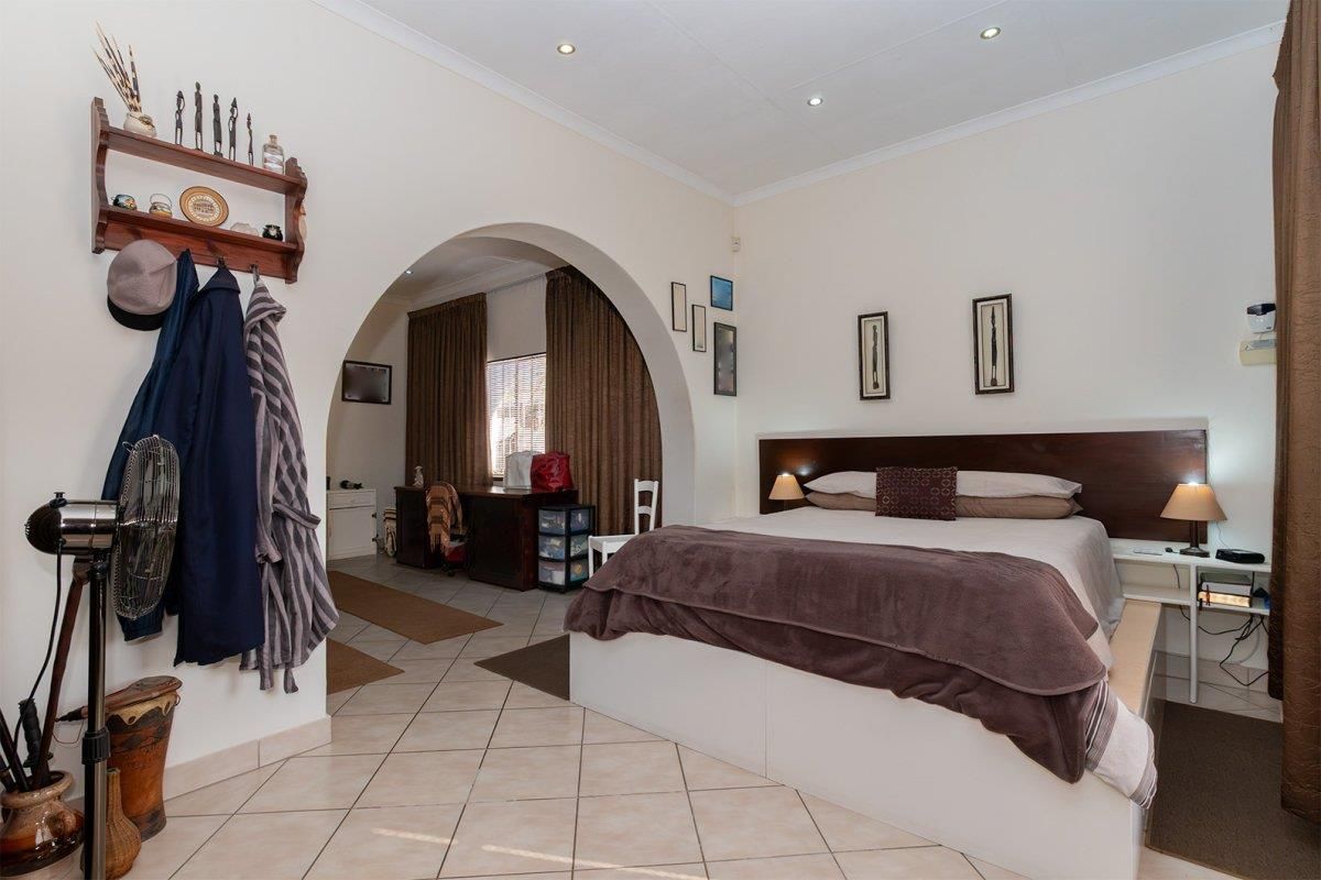 Spacious bedroom featuring tiled flooring, recessed downlighting, and a distinctive architectural archway leading to an adjoining study or dressing area.