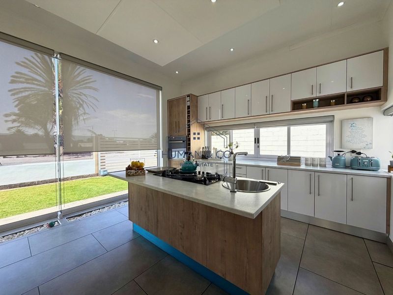 Modern kitchen featuring a central island with gas cooktop and sink, sleek cabinetry, and large windows overlooking the garden.