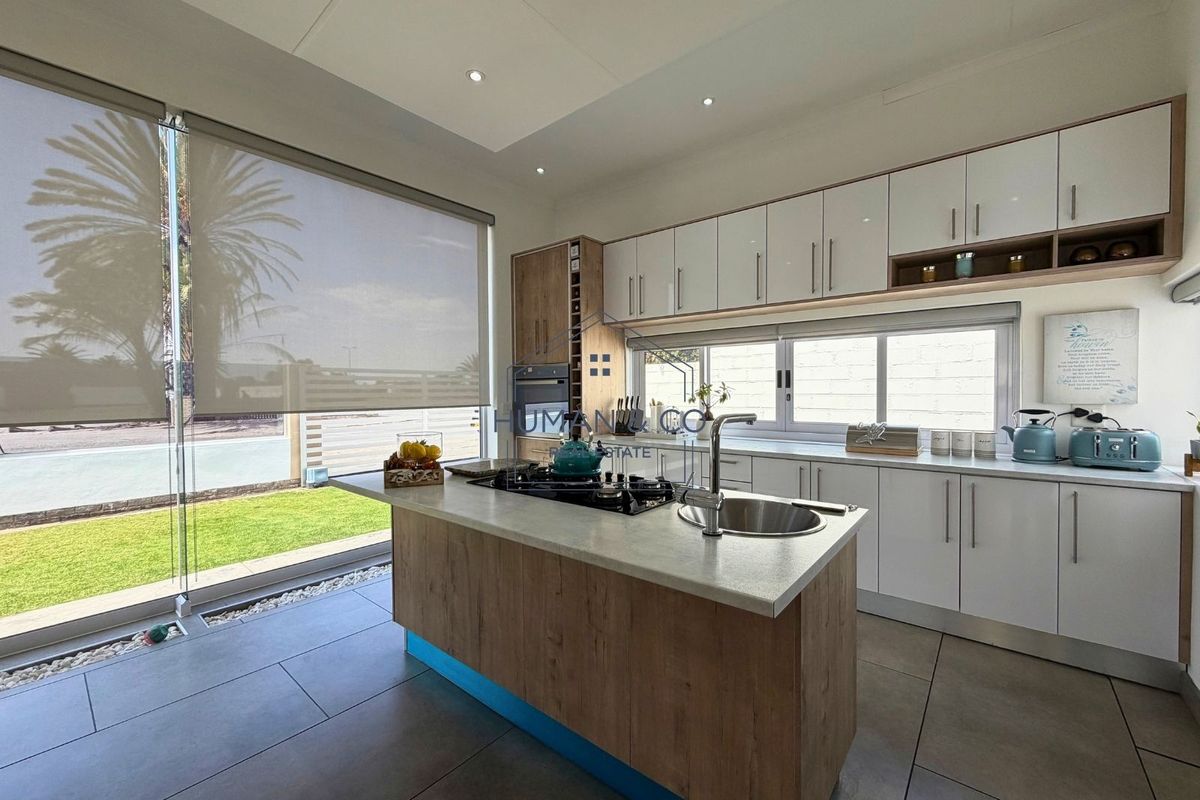 Modern kitchen featuring a central island with gas cooktop and sink, sleek cabinetry, and large windows overlooking the garden.