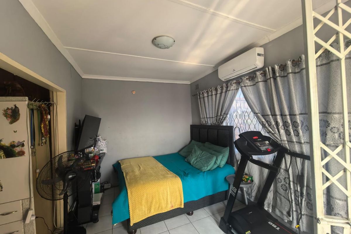 A functional bedroom featuring tiled flooring, a wall-mounted split-system air conditioner, and security window treatments.