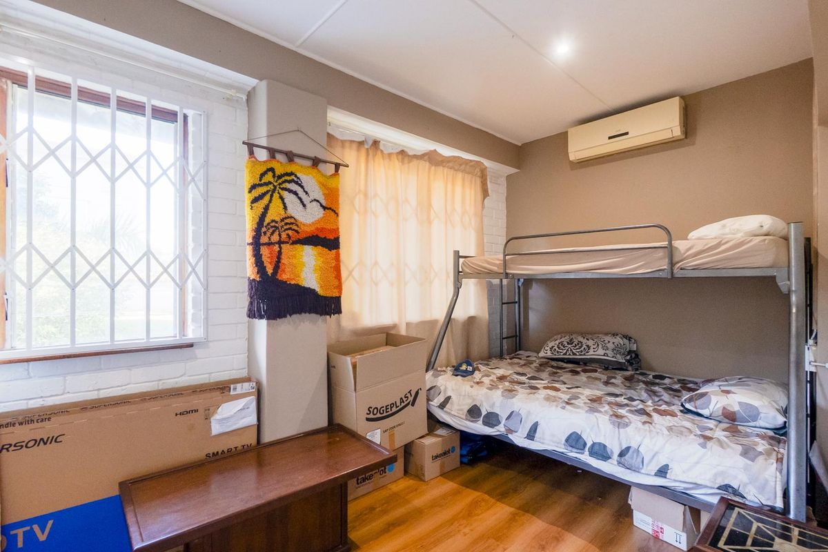 A functional bedroom featuring laminate flooring, a split-system air conditioner, and a security gate on the window.