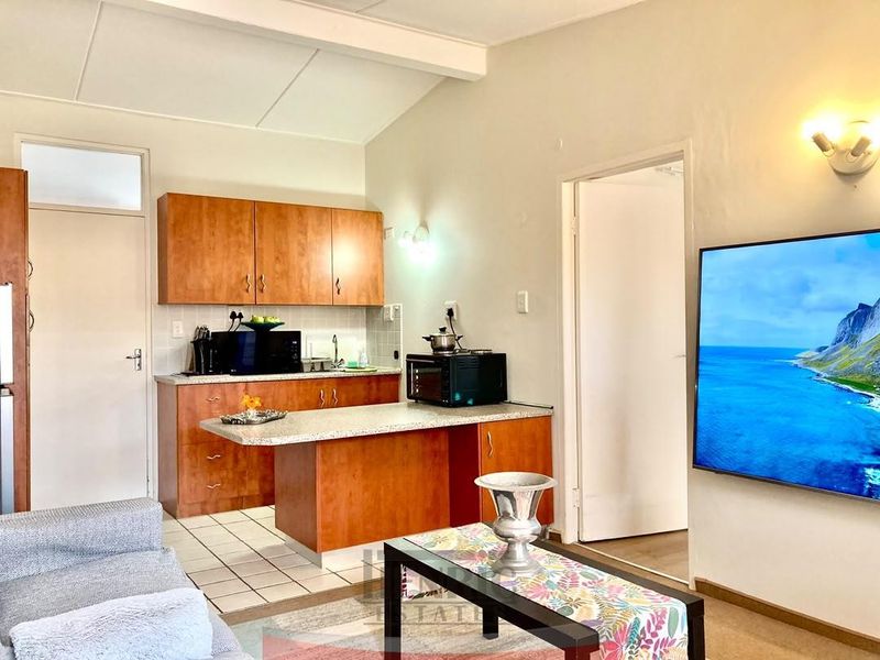 Open-plan living area featuring a compact kitchen with laminate cabinetry, stone-look countertops, and tiled flooring, seamlessly integrated with the main living space.