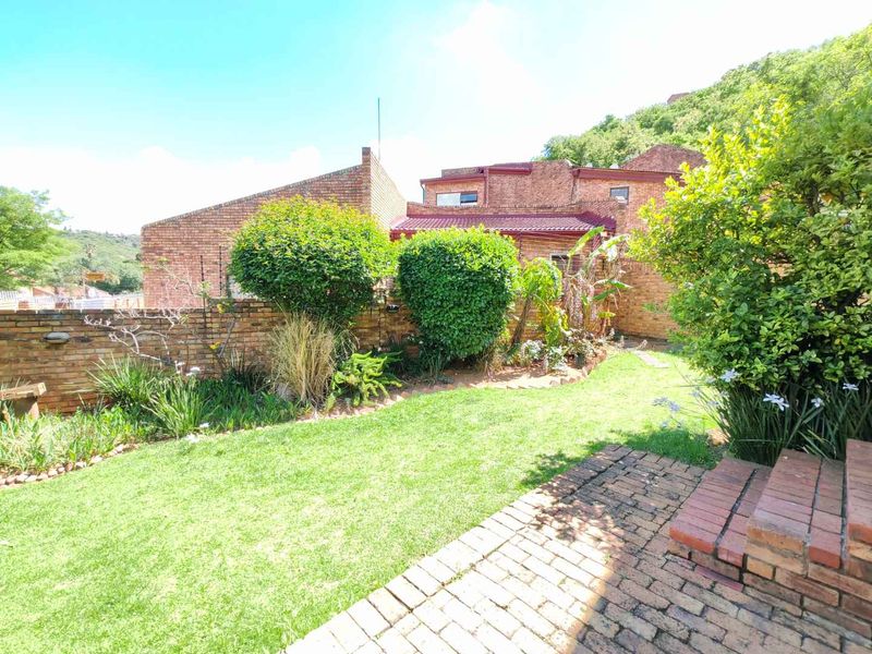 A private rear garden featuring a brick-paved patio, tiered brick steps, and established landscaping against a classic brick townhouse facade.