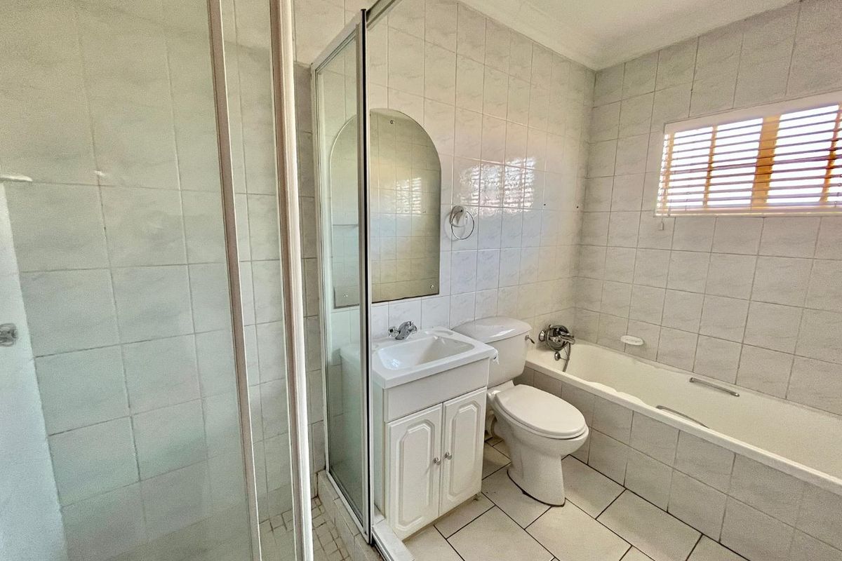 A functional bathroom featuring a separate shower enclosure, a bathtub, a vanity basin, and a toilet, finished with neutral wall and floor tiling.