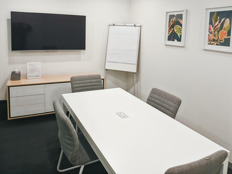 A modern, well-maintained office meeting room featuring a wall-mounted display, built-in storage cabinetry, and integrated desk power connectivity.