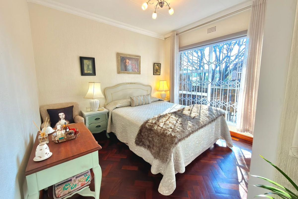 A cozy bedroom featuring classic parquet flooring, crown molding, and a large window with integrated security gate, providing natural light.