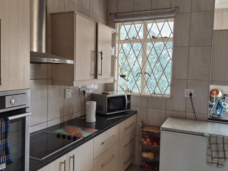 A functional kitchen featuring light wood-tone cabinetry, dark granite countertops, built-in oven, extractor fan, and tiled wall finishes with security bars on the windows.