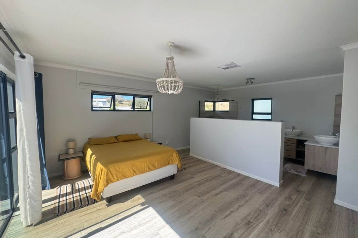Spacious bedroom featuring modern laminate flooring, a partition wall separating the sleeping area from an en-suite vanity with dual vessel sinks.