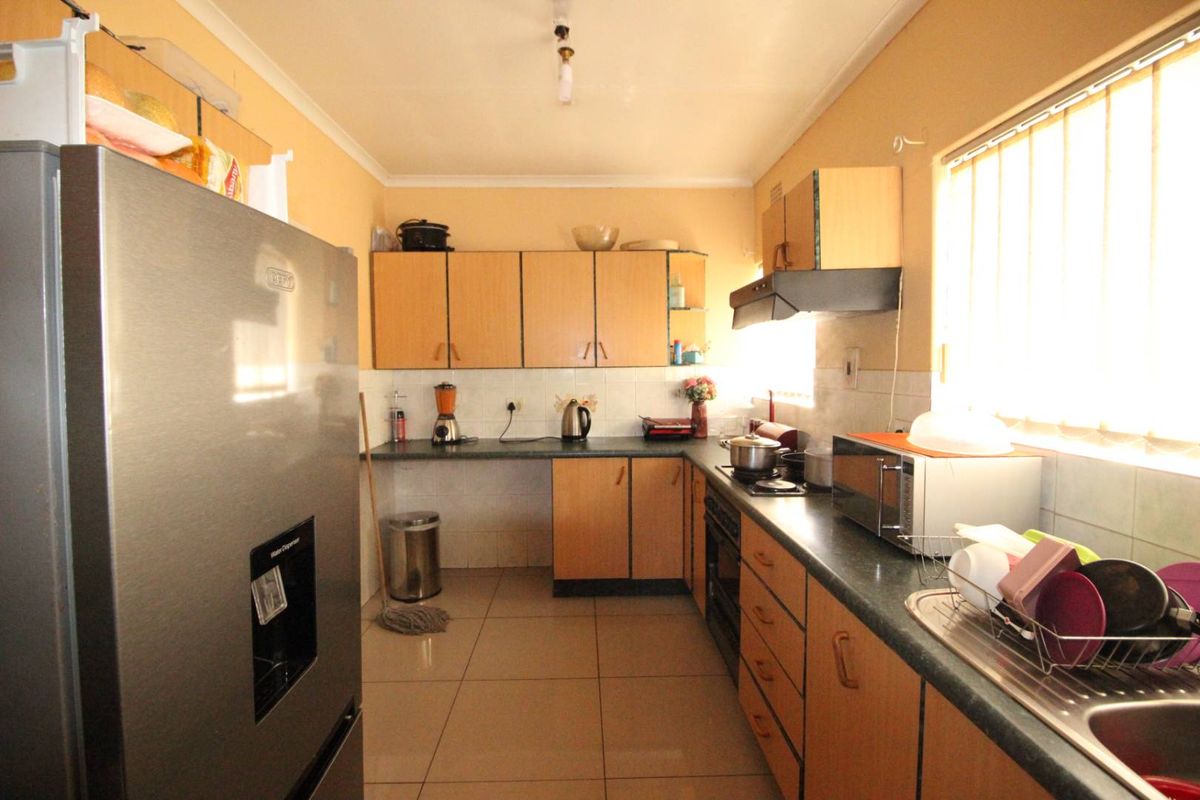A functional kitchen featuring laminate cabinetry, dark countertops, tiled flooring, and a built-in extractor fan, offering a practical layout for daily meal preparation.