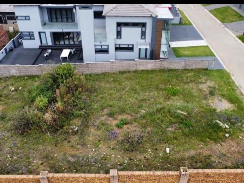 An aerial view of a vacant residential plot featuring boundary walls and adjacent street access in a developed neighborhood.
