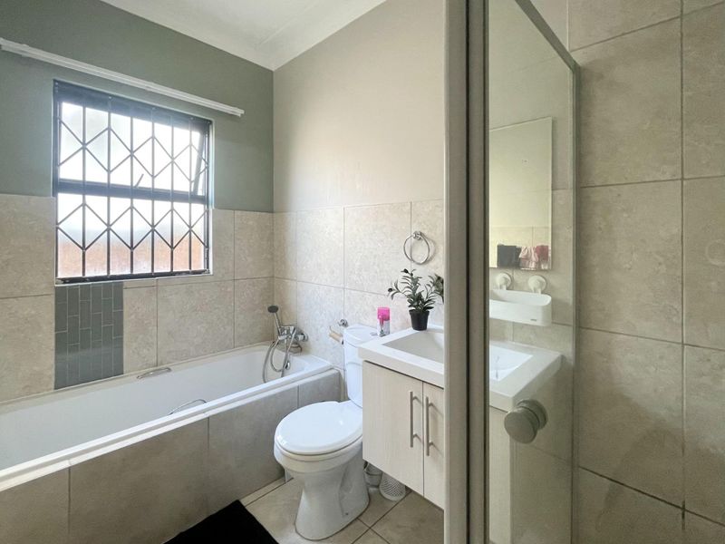 A functional bathroom featuring a bathtub, toilet, and vanity basin with tiled finishes and security bars on the window.