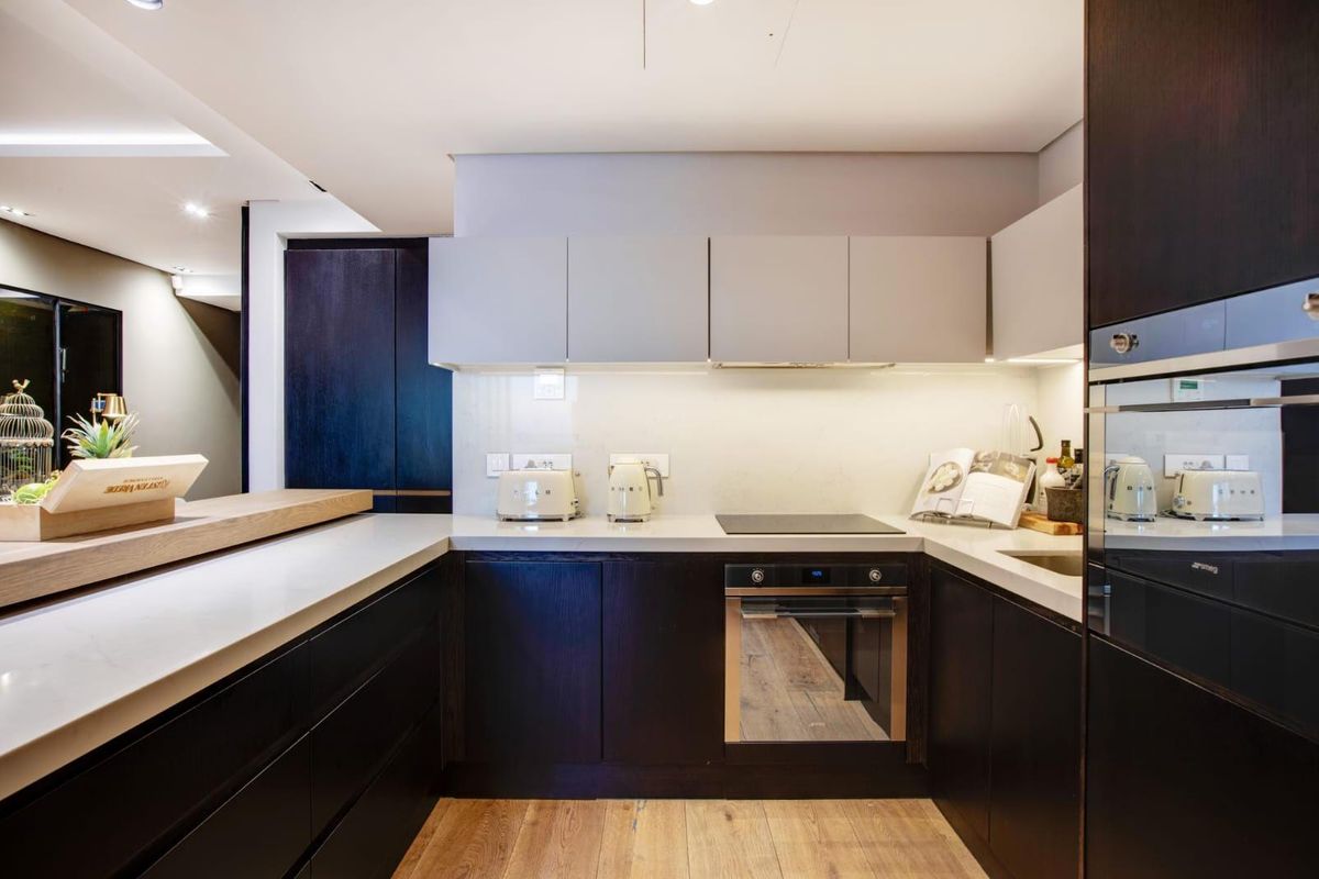 Modern kitchen featuring dark wood cabinetry, light stone countertops, integrated appliances, and high-quality finishes with warm under-cabinet lighting.
