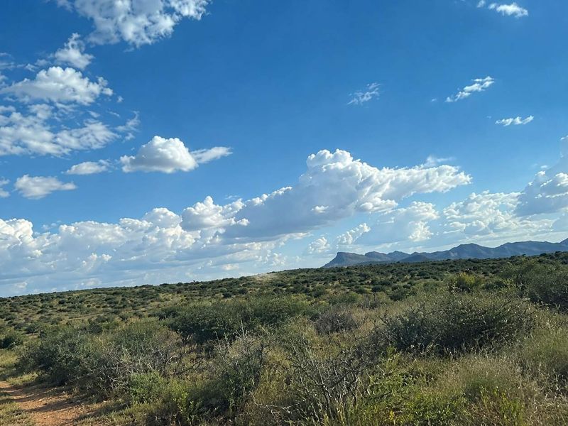 A scenic view of the vacant residential land featuring natural vegetation, a dirt access track, and distant mountain ranges under a clear sky.