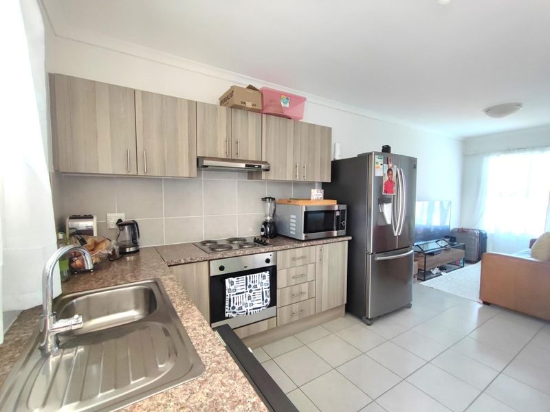Open-plan kitchen and living area featuring light wood-tone cabinetry, tiled flooring, and integrated cooking appliances, creating a functional and connected living space.