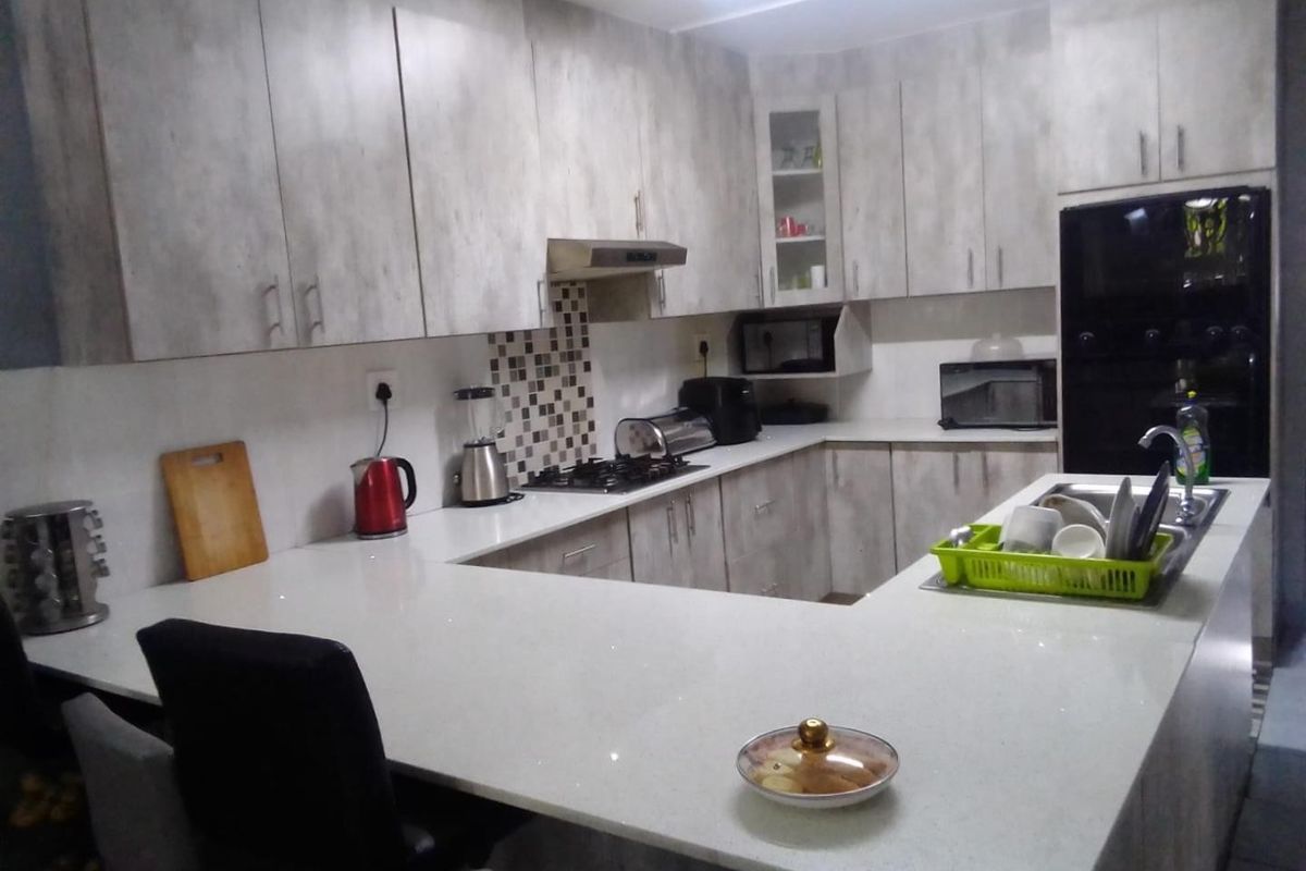 Modern kitchen featuring light wood-grain cabinetry, quartz countertops, a gas hob with extractor, and a breakfast bar peninsula.