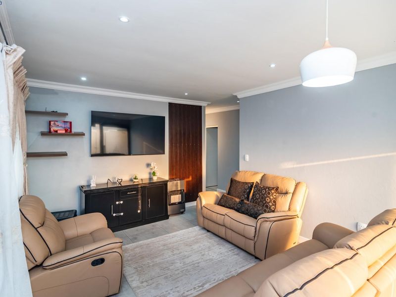 A well-maintained living room featuring recessed downlights, decorative cove molding, and a modern slatted wood accent wall.