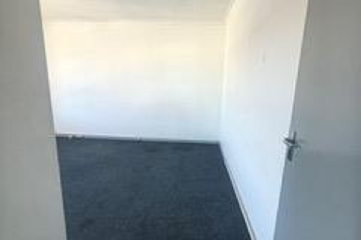 A vacant, neutral-toned office space featuring dark carpeting and a standard internal door, offering a blank canvas for professional use.