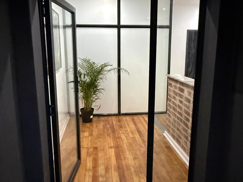 An inviting entrance area featuring polished timber flooring, a rustic brick feature wall, and modern black steel-framed glass partitions.