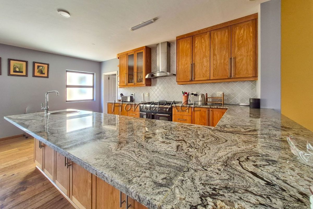 A well-appointed kitchen featuring extensive granite countertops, warm wooden cabinetry, a gas stove with extractor fan, and a modern tiled backsplash.