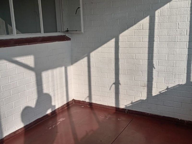 A simple, open balcony area featuring painted brick walls, casement windows, and a concrete floor, offering a blank canvas for outdoor seating.